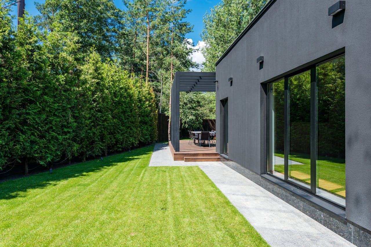 who-we-are Stylish modern house exterior with a lush green yard and outdoor seating area.